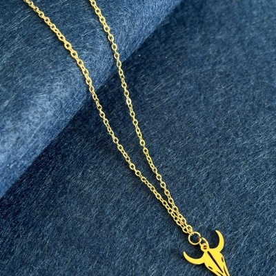 Colar dourado com pendente em forma de crânio de touro sobre tecido azul texturizado