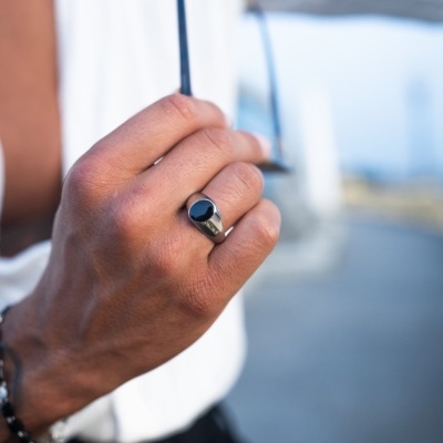 Anel masculino prateado com pedra preta usado na mão direita