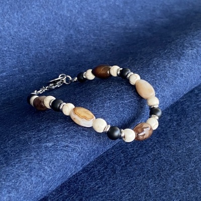 Pulseira com contas em tons castanhos, bege e pretas sobre tecido azul