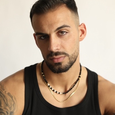 Homem com camisola preta e dois colares contra fundo branco