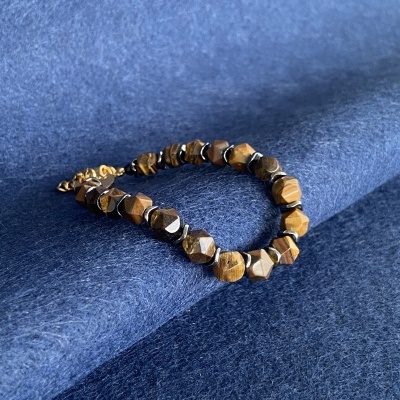 Pulseira facetada castanha e preta com fecho dourado sobre tecido azul