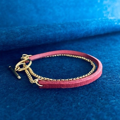 Pulseira de corrente dourada e tira rosa sobre fundo azul texturado