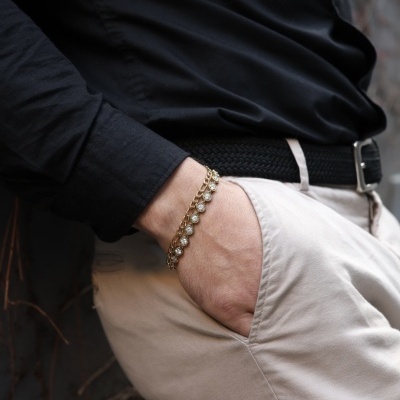 Pulseira dourada com pedras em pulso masculino com roupa preta e bege