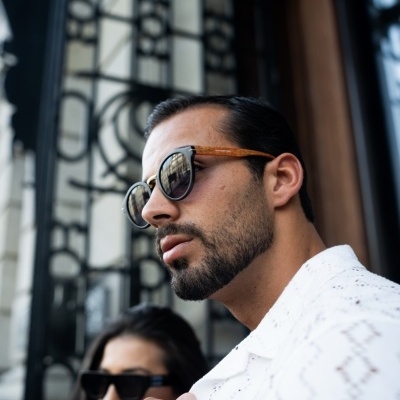 Homem com óculos de sol de armação de madeira e camisa branca padrão, ao ar livre
