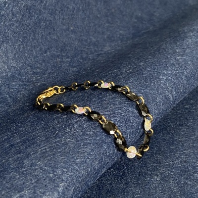 Pulseira com pedras pretas e pedras opacas sobre tecido azul.