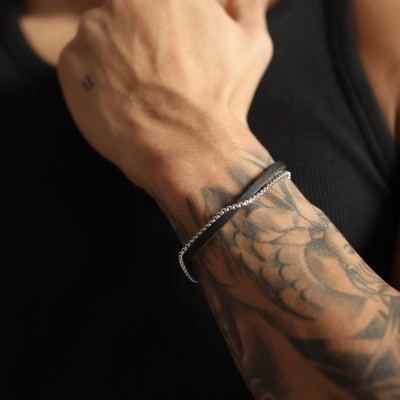 Braço tatuado com pulseira prateada e regata preta