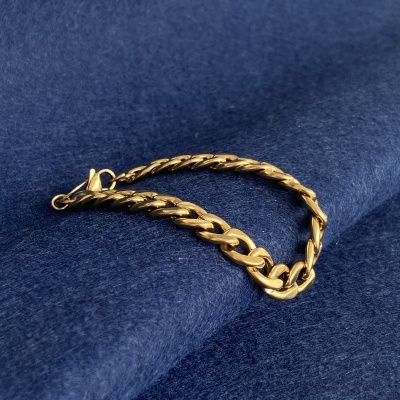 Pulseira dourada de elos grossos sobre tecido azul.