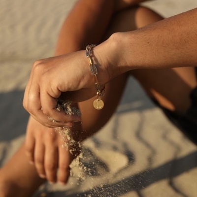 Pulso com pulseira de corrente metálica dourada segurando areia na praia