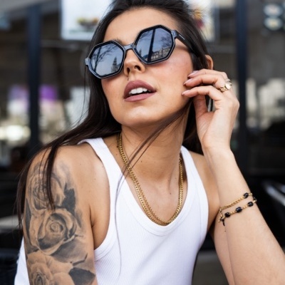 Mulher com tatuagem de flores no braço e óculos de sol pretos numa esplanada