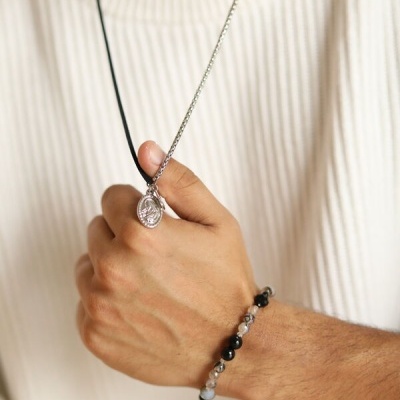 Colar prateado com pingente redondo e pulseira de contas pretas e cinzentas.