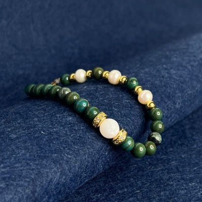 Pulseira com contas verdes, pérolas brancas e detalhes dourados sobre tecido azul escuro