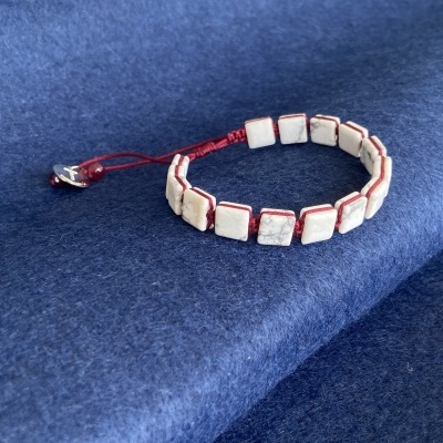 Pulseira com contas quadradas brancas e fio vermelho sobre tecido azul