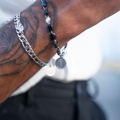 Pulso com três pulseiras incluindo contas pretas e brancas, corrente prateada e pulseira metálica com detalhes