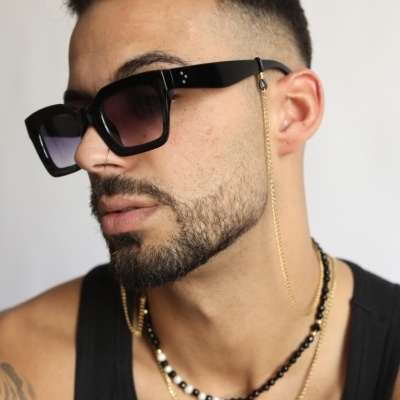 Homem com óculos de sol pretos, corrente dourada e colares, fundo branco