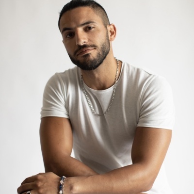 Homem com t-shirt branca, colares prateados e pulseira de contas