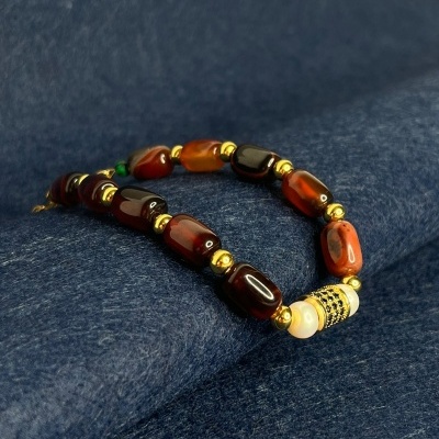 Colar ou pulseira com contas castanhas, douradas e uma conta branca decorada sobre tecido azul