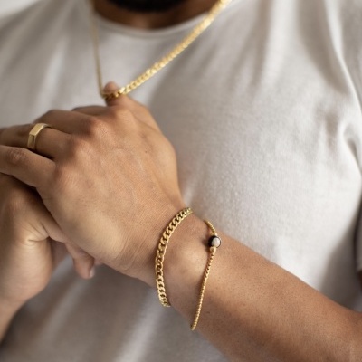 Pulso de homem com duas pulseiras douradas e anel dourado