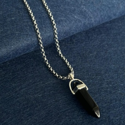 Colar prateado com pendente de cristal preto sobre fundo azul escuro