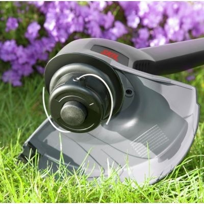 Aparelho aparador de relva em relva verde com flores cor-de-rosa