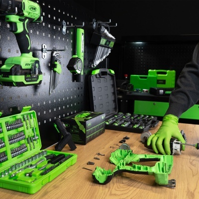 Ferramentas elétricas e manuais verdes e pretas organizadas numa parede perfurada e numa bancada de madeira clara