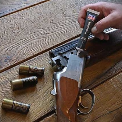 Arma de fogo com cartuchos e tubo de cola Liqui Wrench numa superfície de madeira