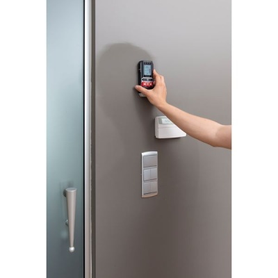 Mão a usar medidor digital de distância numa parede cinzenta perto de porta de vidro