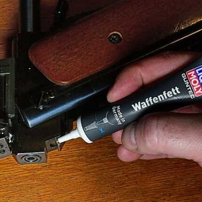 Mão a aplicar lubricante LIQUI MOLY Waffenfett em arma com cabo de madeira