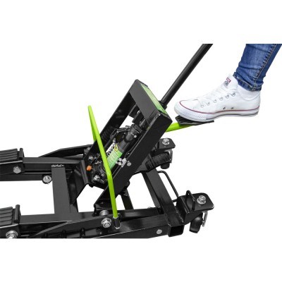 Macaco hidráulico metálico preto e verde com pé a pressionar o pedal e ténis branco em fundo branco