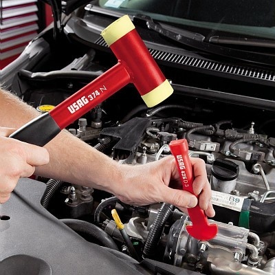 Martelo de borracha vermelho e amarelo com cabo preto e vermelho com texto USAG 374 N em uso em motor de carro