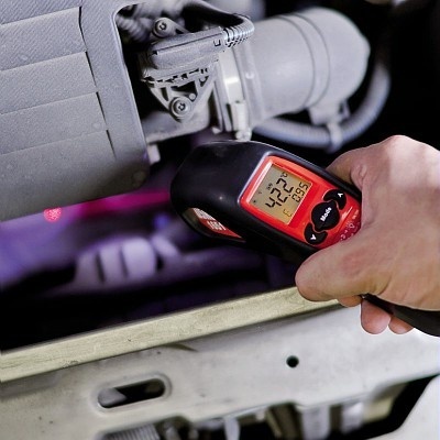 Termómetro digital infravermelho vermelho e preto a medir temperatura num motor de automóvel.