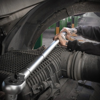 Mão usando chave de catraca metálica num motor de carro com peças em plástico e metal