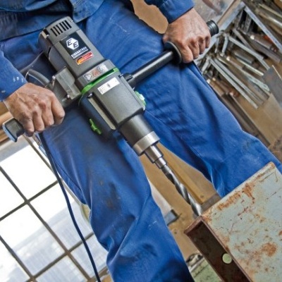 Pessoa com macacão azul a usar berbequim elétrico numa oficina