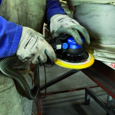 Lixadora elétrica em uso com luvas e avental em ambiente industrial