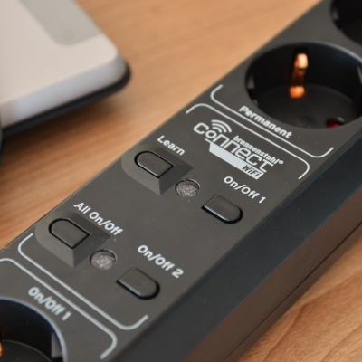 Régua de tomadas preta com botões e texto branco sobre mesa de madeira