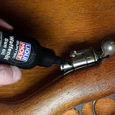 Frasco de lubrificante Liqui Moly Gun Oil a ser aplicado numa arma de fogo de madeira