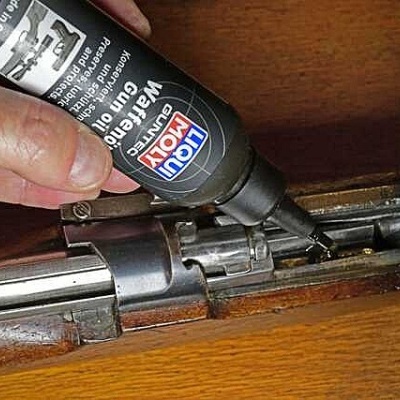 Frasco preto de óleo para armas LIQUI MOLY e arma calibre .22 sobre madeira