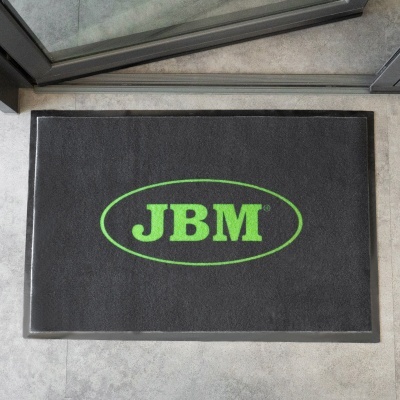 Tapete preto com logo verde JBM colocado no chão de entrada de porta de vidro