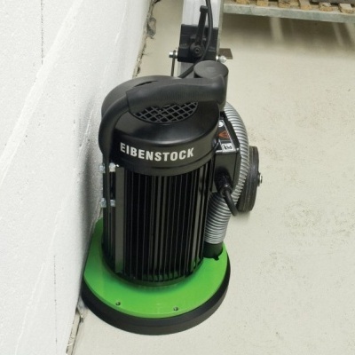 Raspa piso elétrico Eibenstock preto e verde em chão interior cinza junto a parede branca