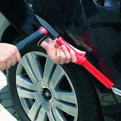 Ferramenta metálica com cabo preto e vermelho para destrancar carro junto a roda de carro preto