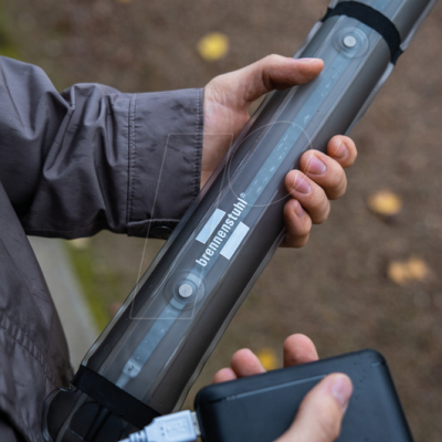 Objeto cilíndrico transparente com texto brennenstuhl, segurado por pessoa com casaco cinzento