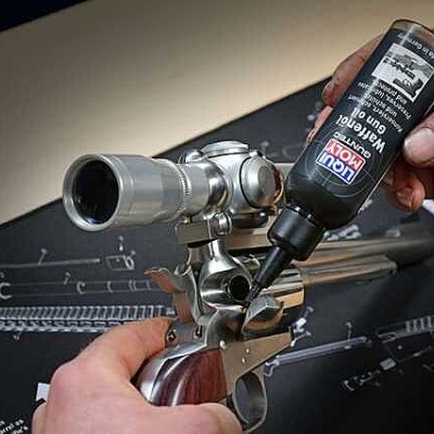 Frasco preto de óleo lubrificante a ser aplicado numa arma com luneta, sobre tapete de limpeza