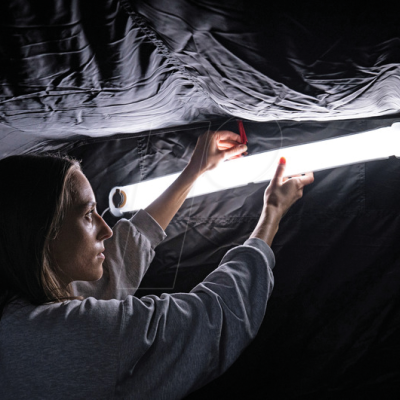 Mulher segurando uma luz tubular LED branca contra um fundo de tecido preto.
