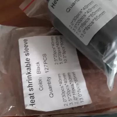 Pacotes transparentes com mangas termorretráteis pretas etiquetadas, sobre mesa de madeira