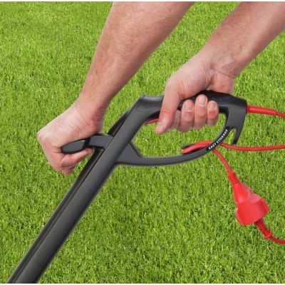 Cabo preto de ferramenta elétrica de jardim com fio vermelho sobre relva verde