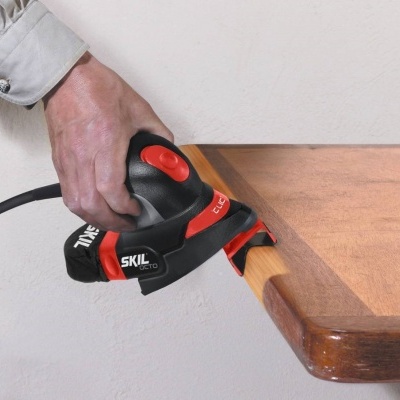 Lixadora elétrica preta e vermelha a lixar borda de mesa de madeira clara