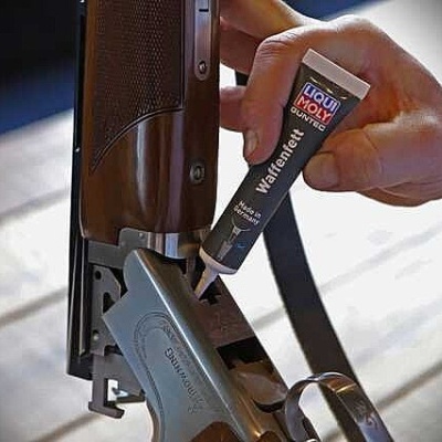Mão aplicando lubrificante LIQUI MOLY Waffenfett numa espingarda de madeira e metal