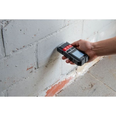 Medidor digital preto com botões vermelhos junto a parede branca de blocos de cimento