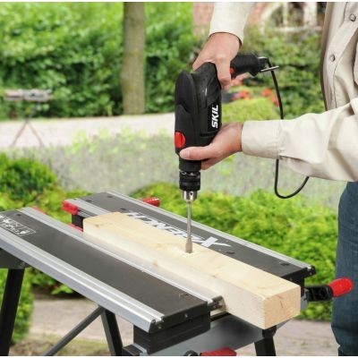 Furadeira preta a perfurar madeira numa bancada exterior