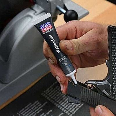Pessoa a aplicar Liqui Moly GunTec numa arma preta em oficina