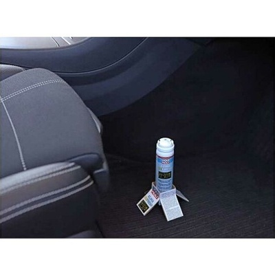 Frasco com rótulo azul e branco no chão do carro entre o banco e painel